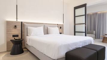 Una habitación de hotel moderna con una cama grande, una mesita de noche, un pequeño pupitre, un sofá y un ventanal con cortinas.