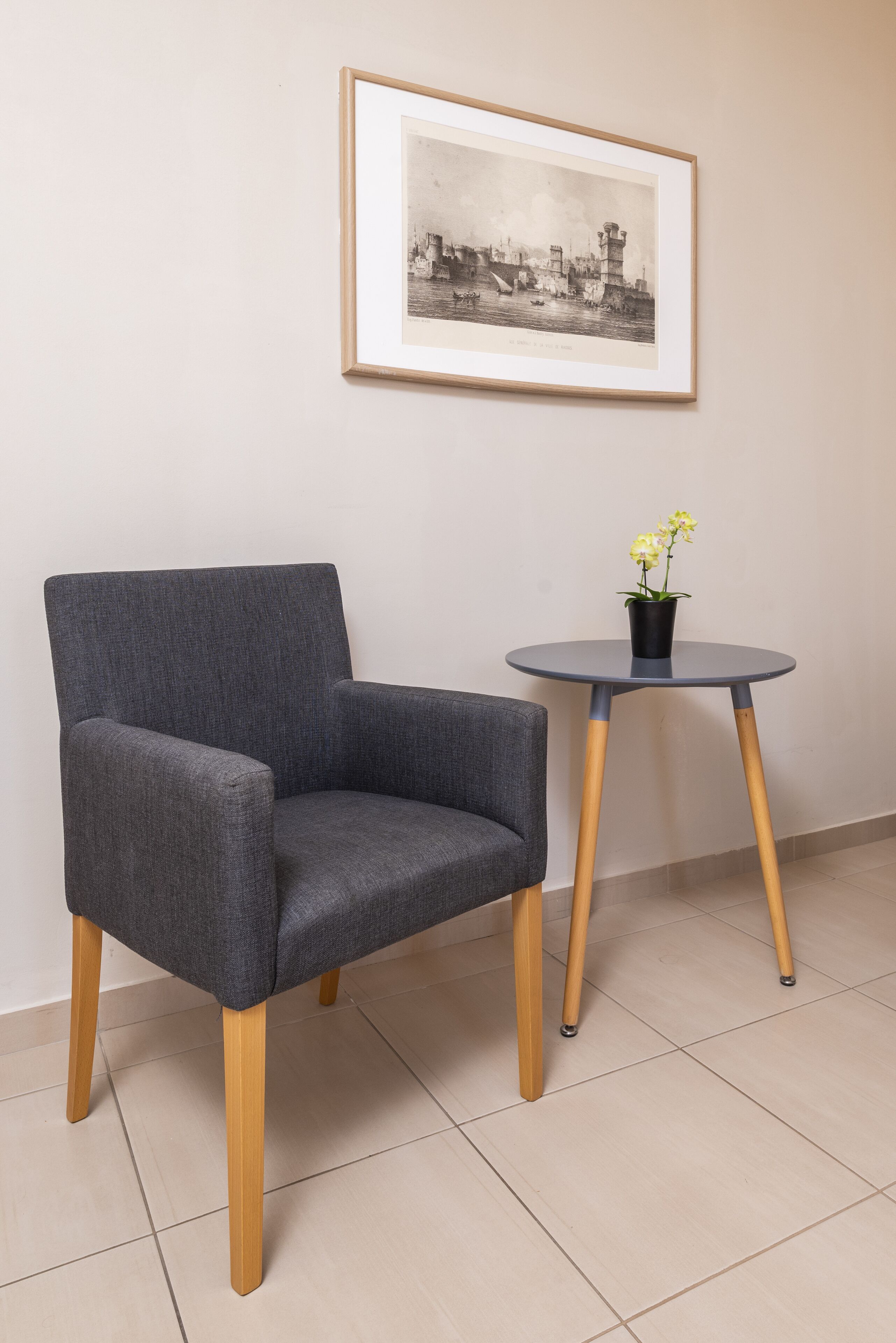 Un sillón gris con patas de madera, una mesita redonda con una planta en maceta y una fotografía en blanco y negro enmarcada en la pared.