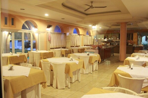 A dining area with round tables, white tablecloths, and beige chairs. - Faliraki Bay (Rhodes)