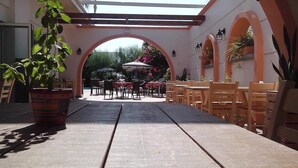 An outdoor patio area with tables and chairs, a potted plant, and an archway leading to another section. - Faliraki Bay (Rhodes)