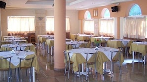 A dining area with multiple round tables covered with yellow tablecloths, arranged in rows. - Faliraki Bay (Rhodes)