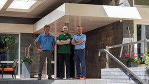 Three men standing in front of a building with a modern architectural design, featuring a glass entrance and a staircase.