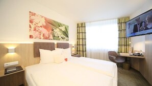 A hotel room with a large bed, a desk with a chair, a television, and a painting on the wall.