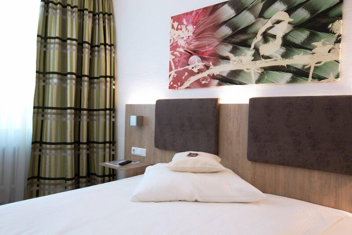Een hotelkamer met een bed, hoofdbord, kussen, nachtkastje, afstandsbediening en een kunstwerk aan de muur.