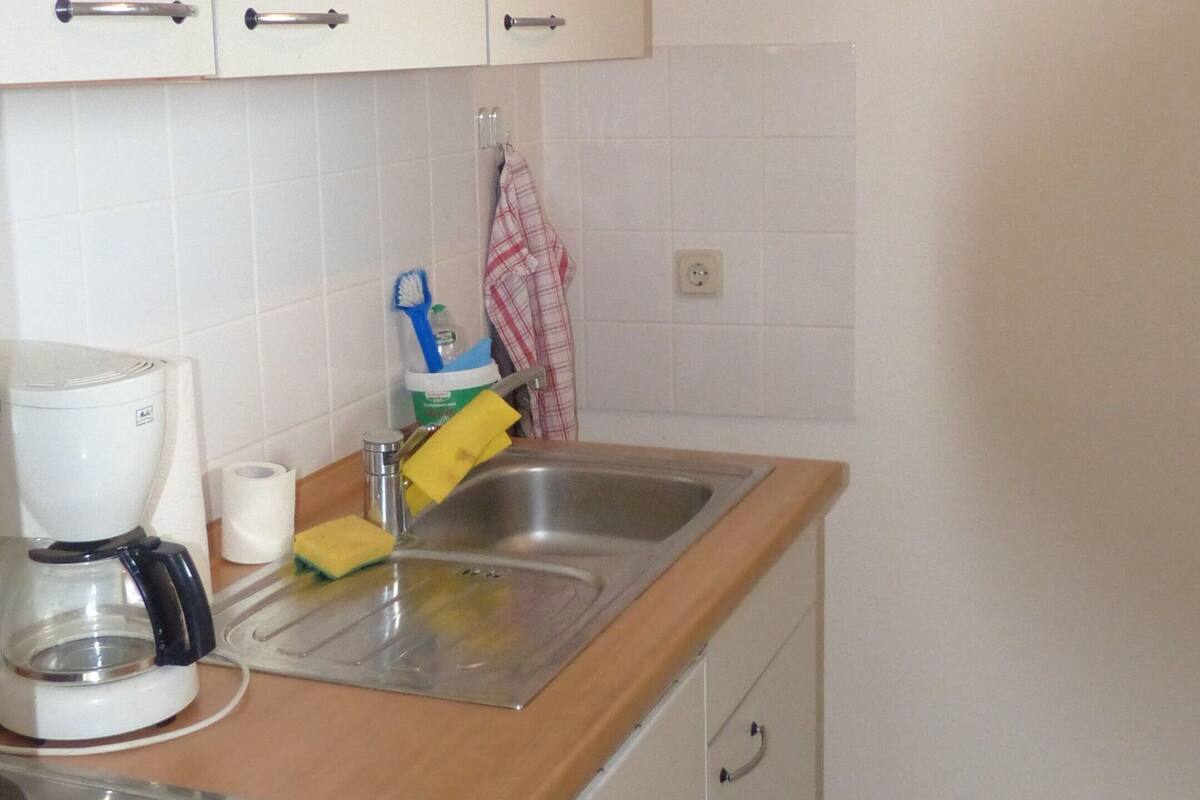 Een keuken met witte kastjes, een roestvrijstalen spoelbak, een koffiezetapparaat en een klein fornuis.