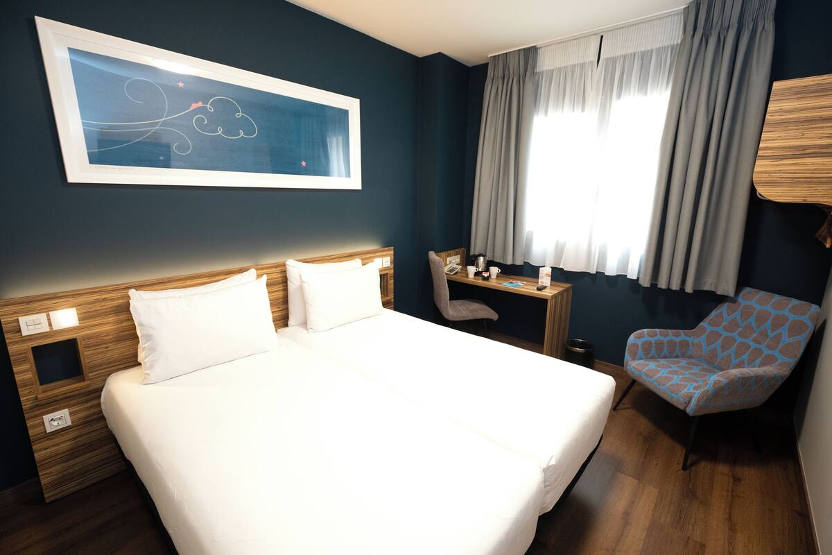 Une chambre d’hôtel avec un grand lit, un bureau, une chaise et une fenêtre avec des rideaux.