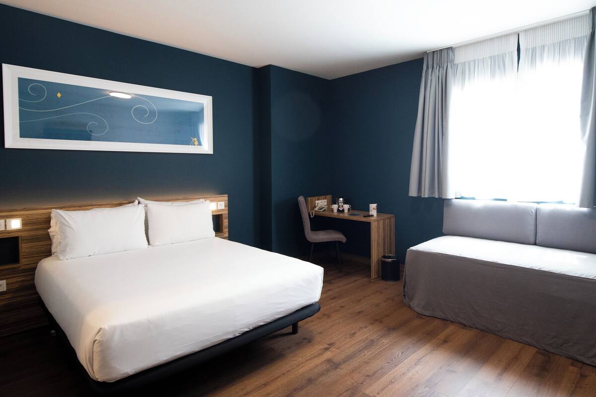 Une chambre d’hôtel avec un grand lit, un canapé, un bureau et une fenêtre avec des rideaux.