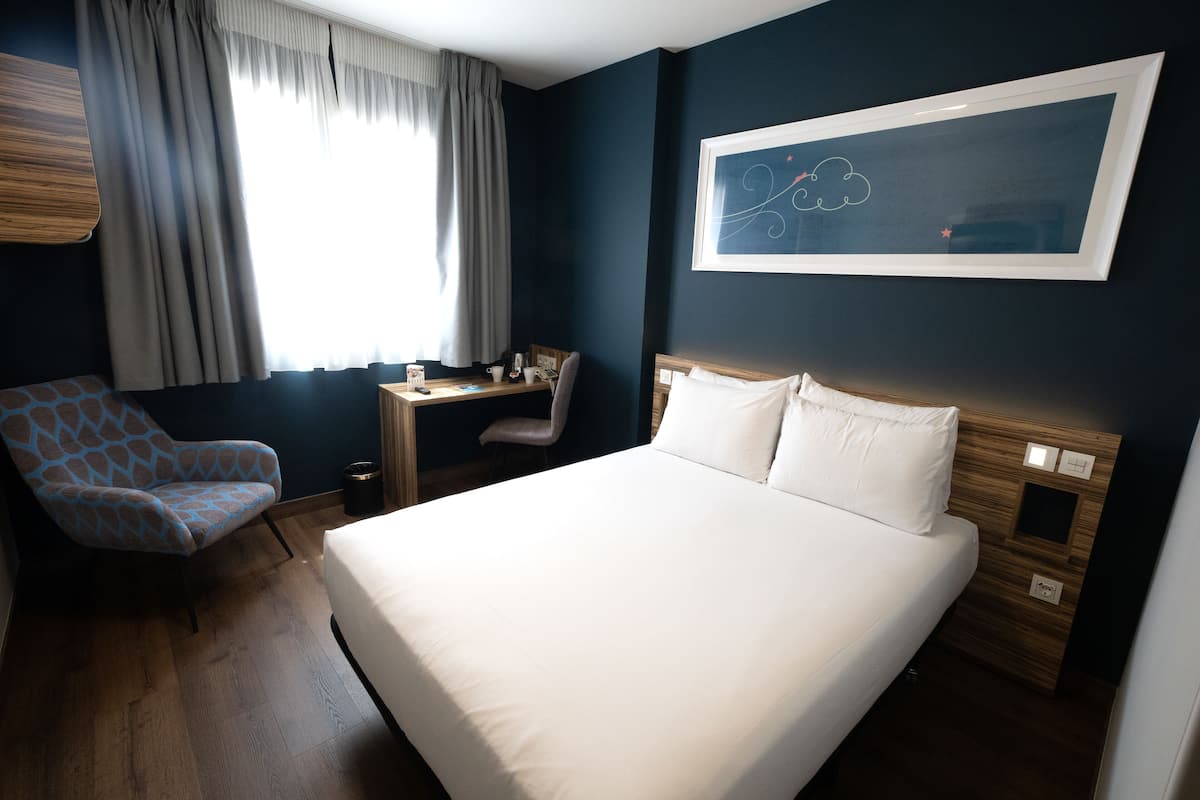 Une chambre d’hôtel avec un grand lit, un bureau, une chaise et une fenêtre avec des rideaux.