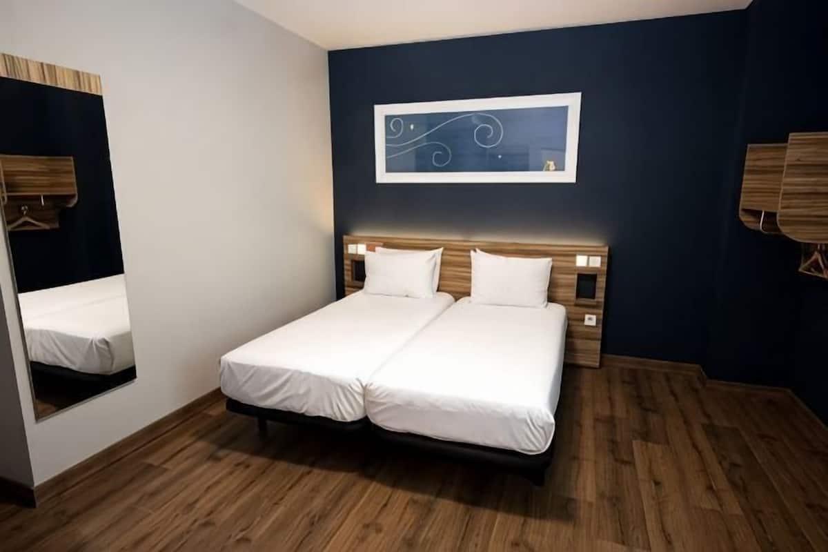 Un lit double avec du linge de lit blanc, un mur d’accent bleu foncé et une œuvre d’art abstraite encadrée au-dessus du lit.