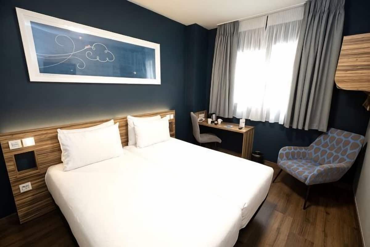 Une chambre d’hôtel avec un grand lit, un bureau, une chaise et une fenêtre avec des rideaux.