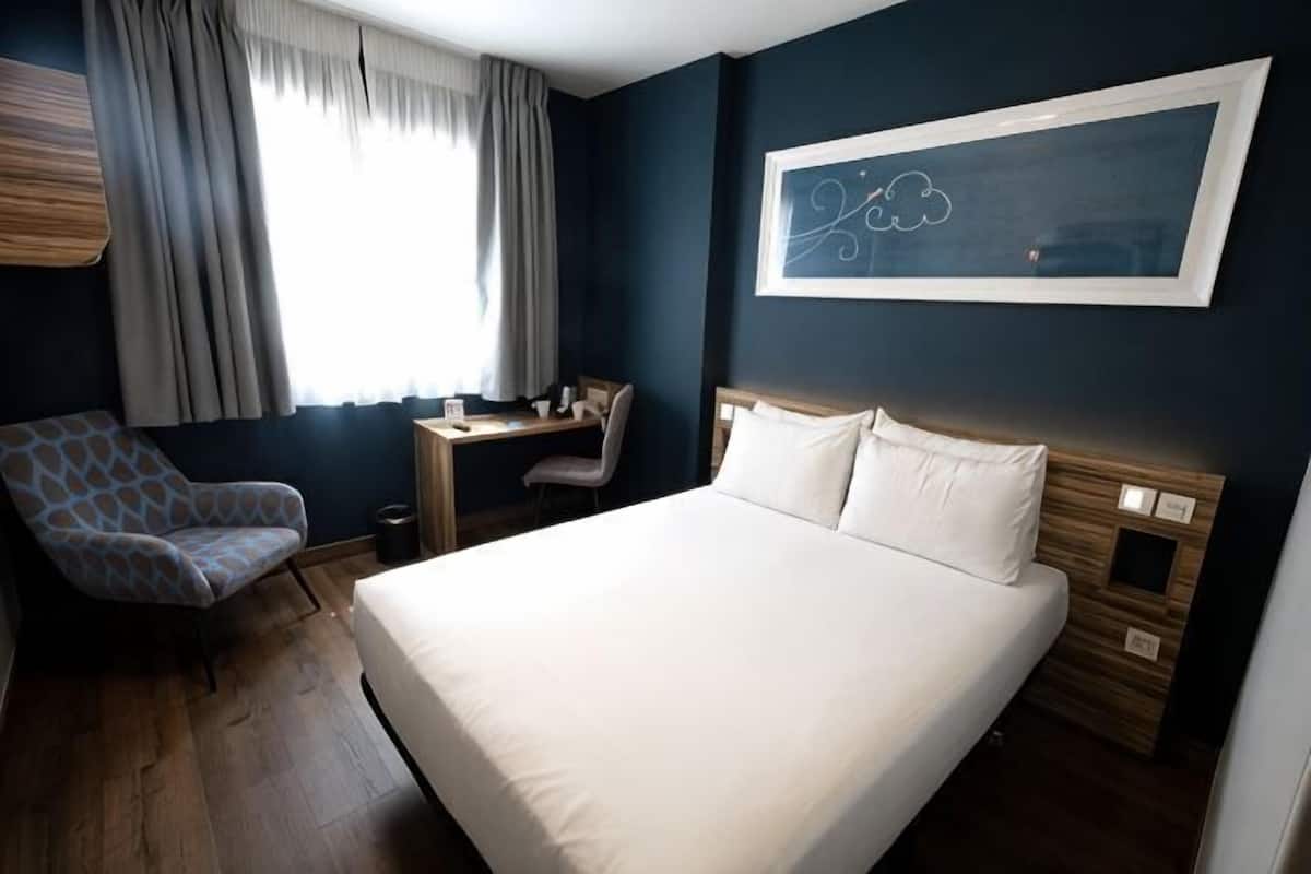 Une chambre d’hôtel avec un lit, un bureau, une chaise et une fenêtre avec des rideaux.