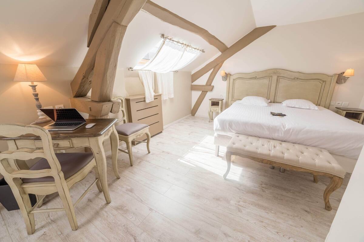 A bedroom with a bed, bedside table, lamp, and a desk with a chair.