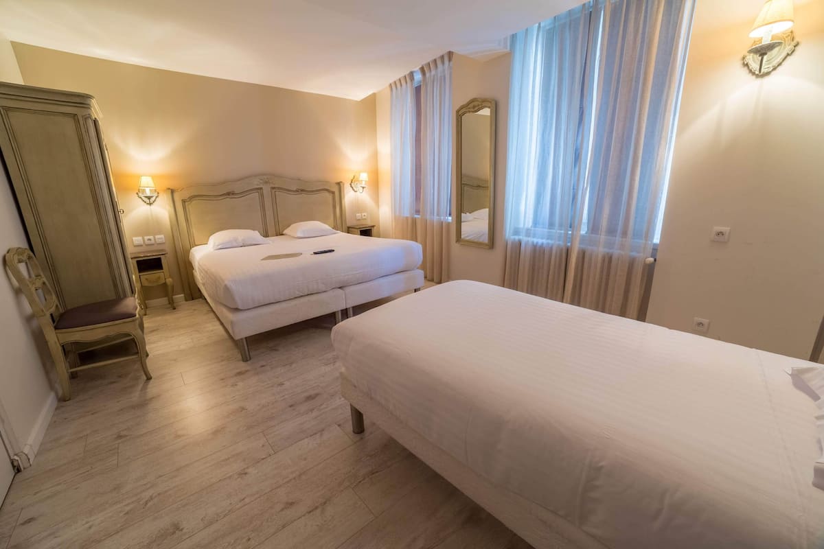 A hotel room with two beds, a chair, a mirror, and a nightstand with a lamp.