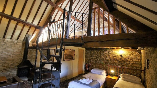 A rustic room with a loft bed, stone walls, a fireplace, and a wooden staircase. - The Kings Arms Chipping Norton (Chipping Norton)