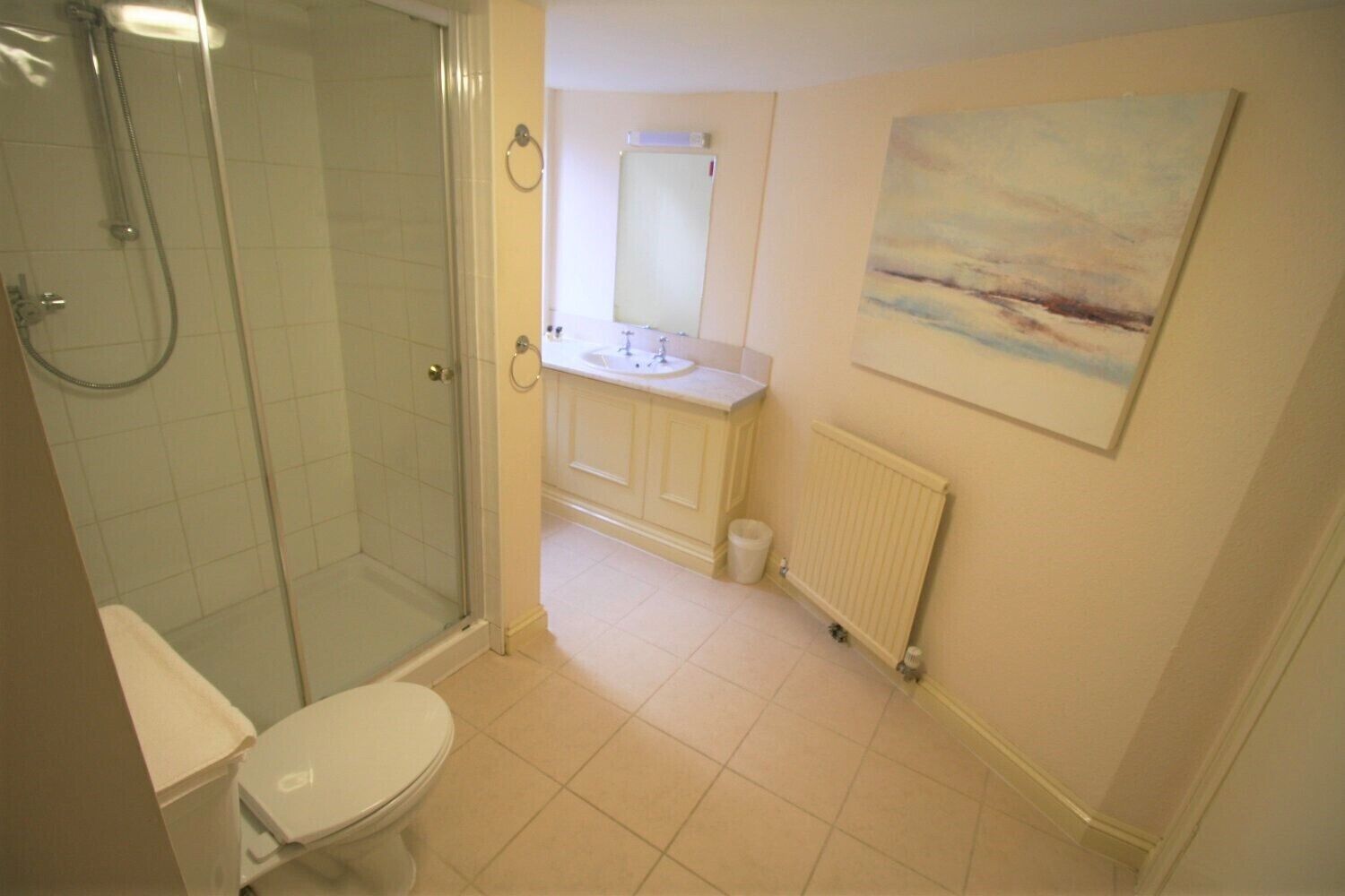 A bathroom with a glass-enclosed shower, a toilet, a sink, and a radiator.