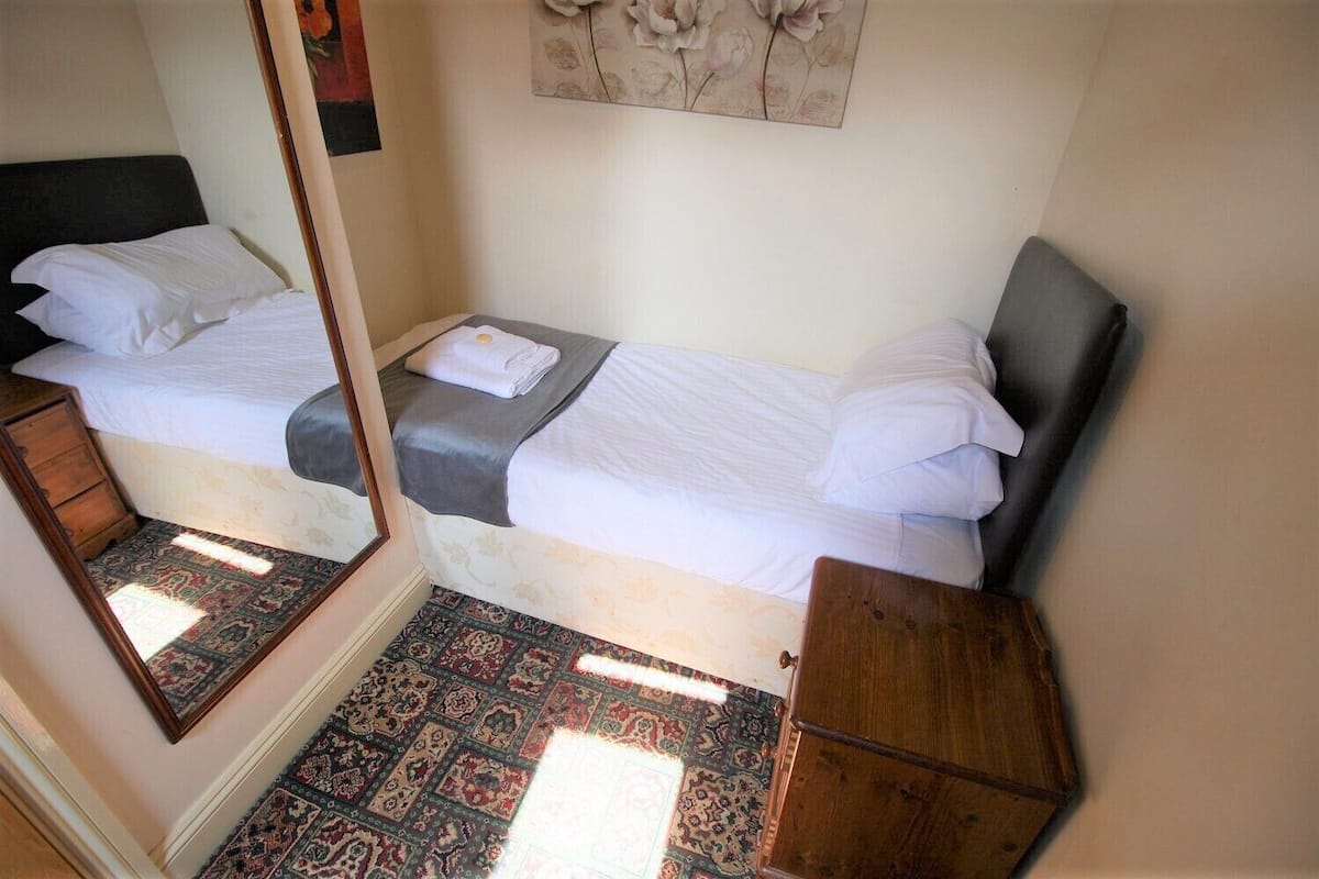 A small, cozy room with two beds, a mirror, a rug, and a painting on the wall.