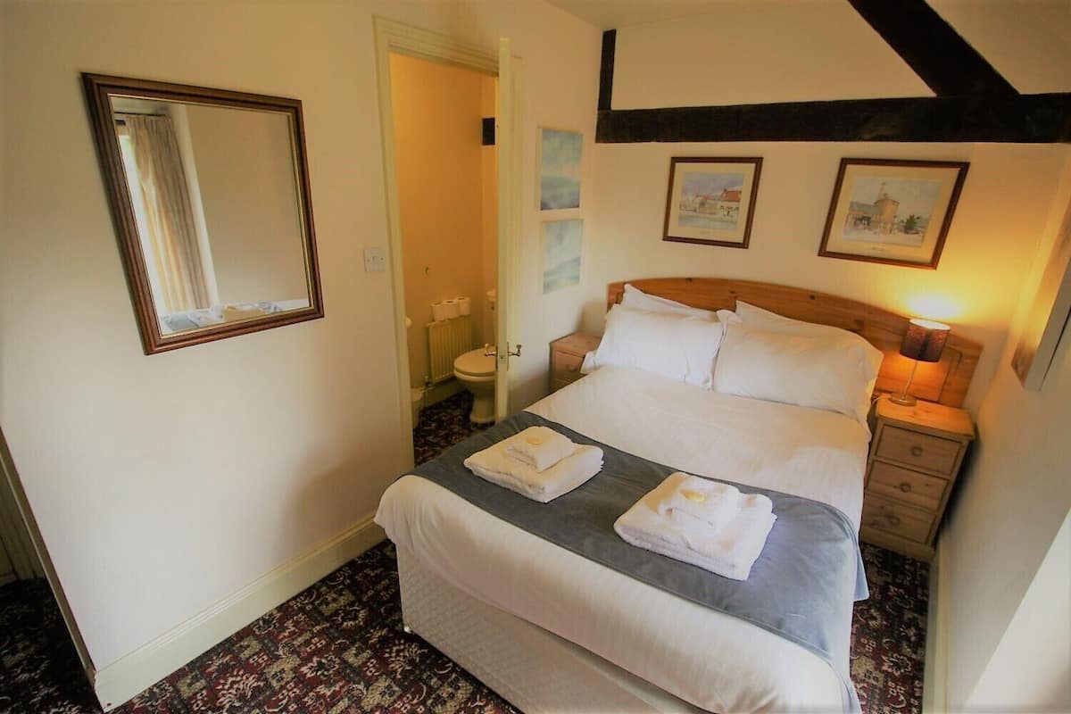 A neatly arranged bedroom with a bed, bedside tables, a mirror, and framed pictures on the wall.