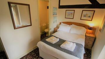 A neatly arranged bedroom with a bed, bedside tables, a mirror, and framed pictures on the wall.