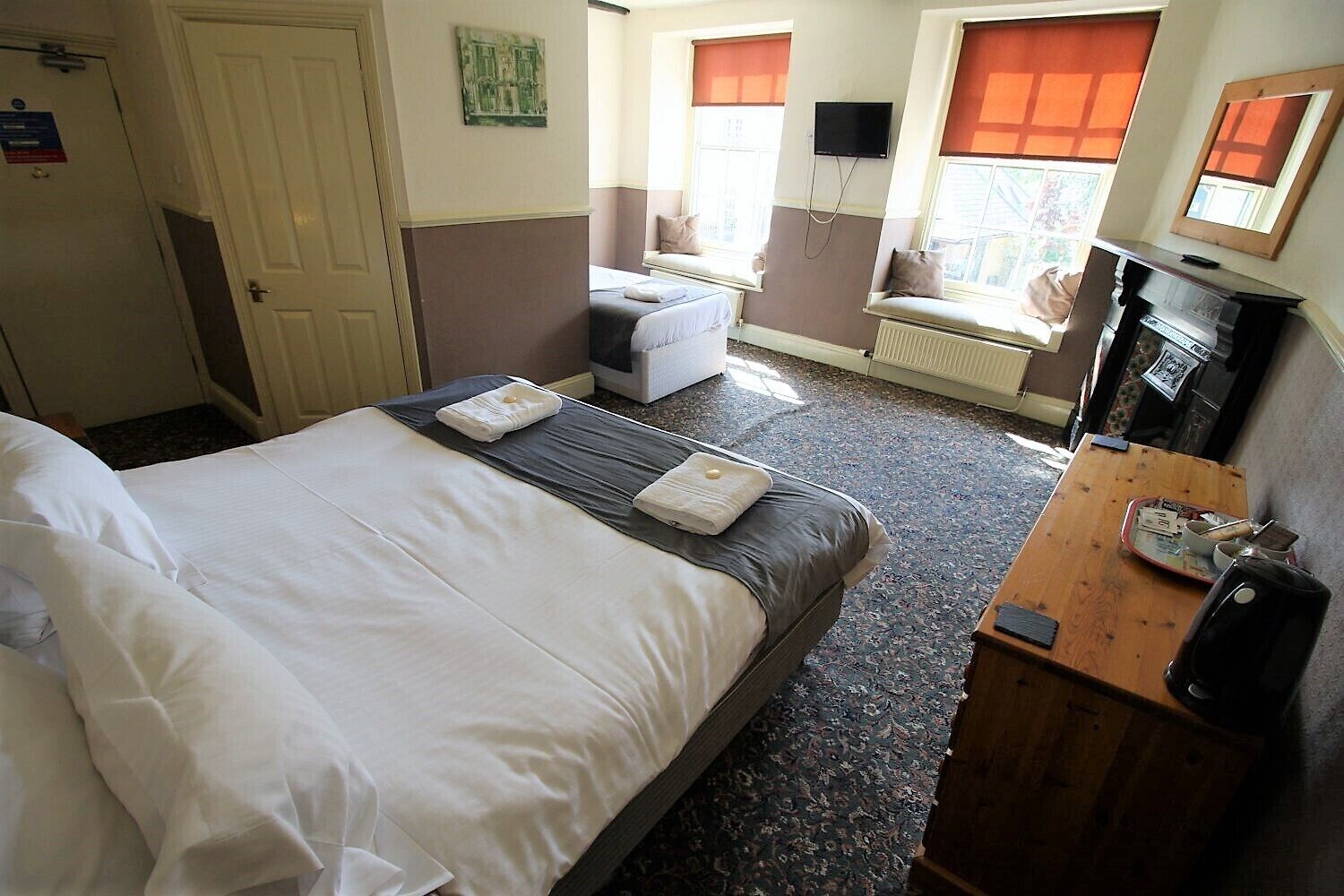 A hotel room with two beds, a sofa bed, a small table, a TV, and a radiator.