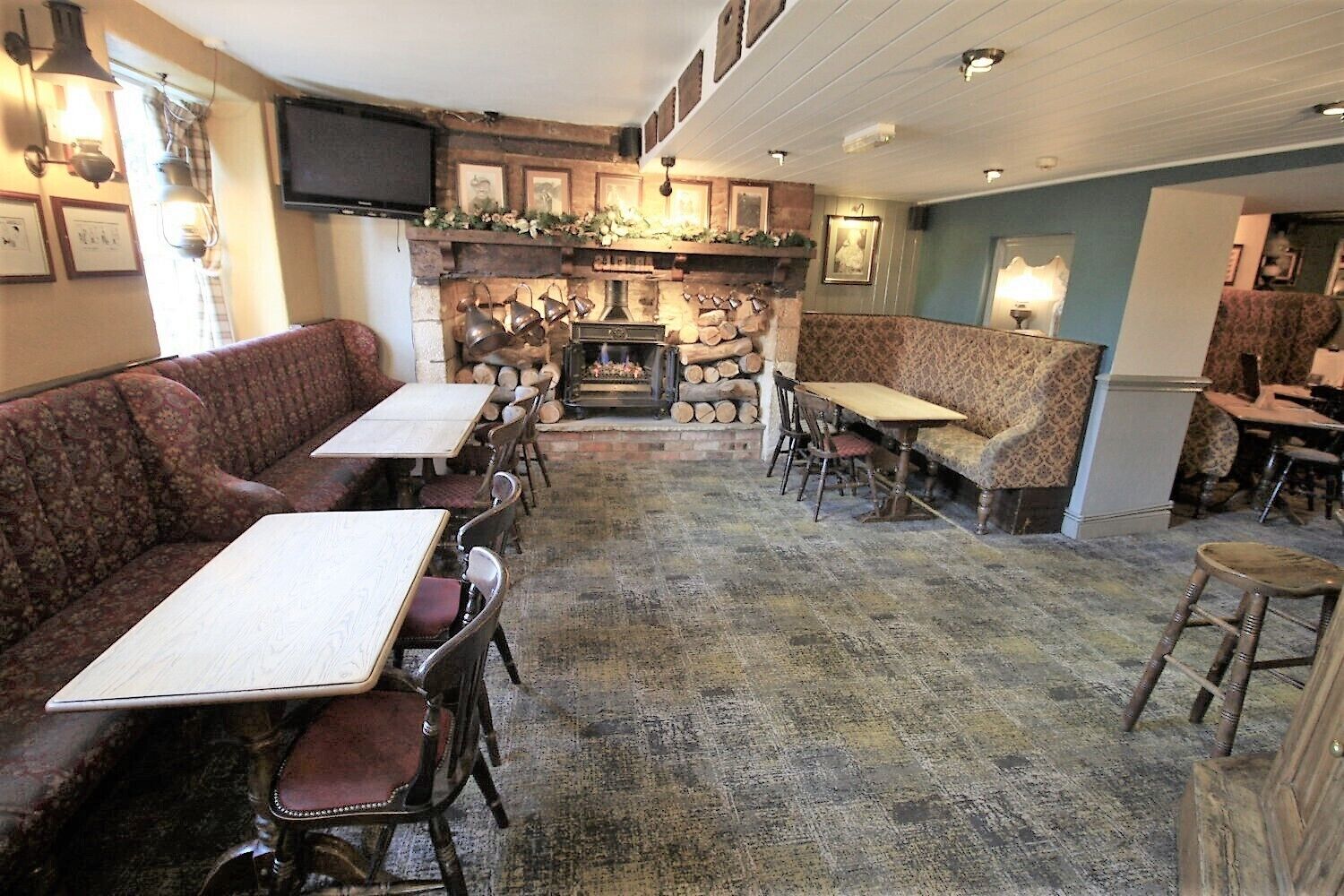 Um restaurante acolhedor com mesas e bancos de madeira, uma lareira e quadros nas paredes.