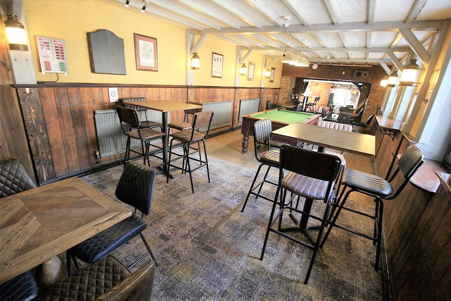 Una sala de billar con mesas y sillas de madera, una mesa de billar y una zona de bar.