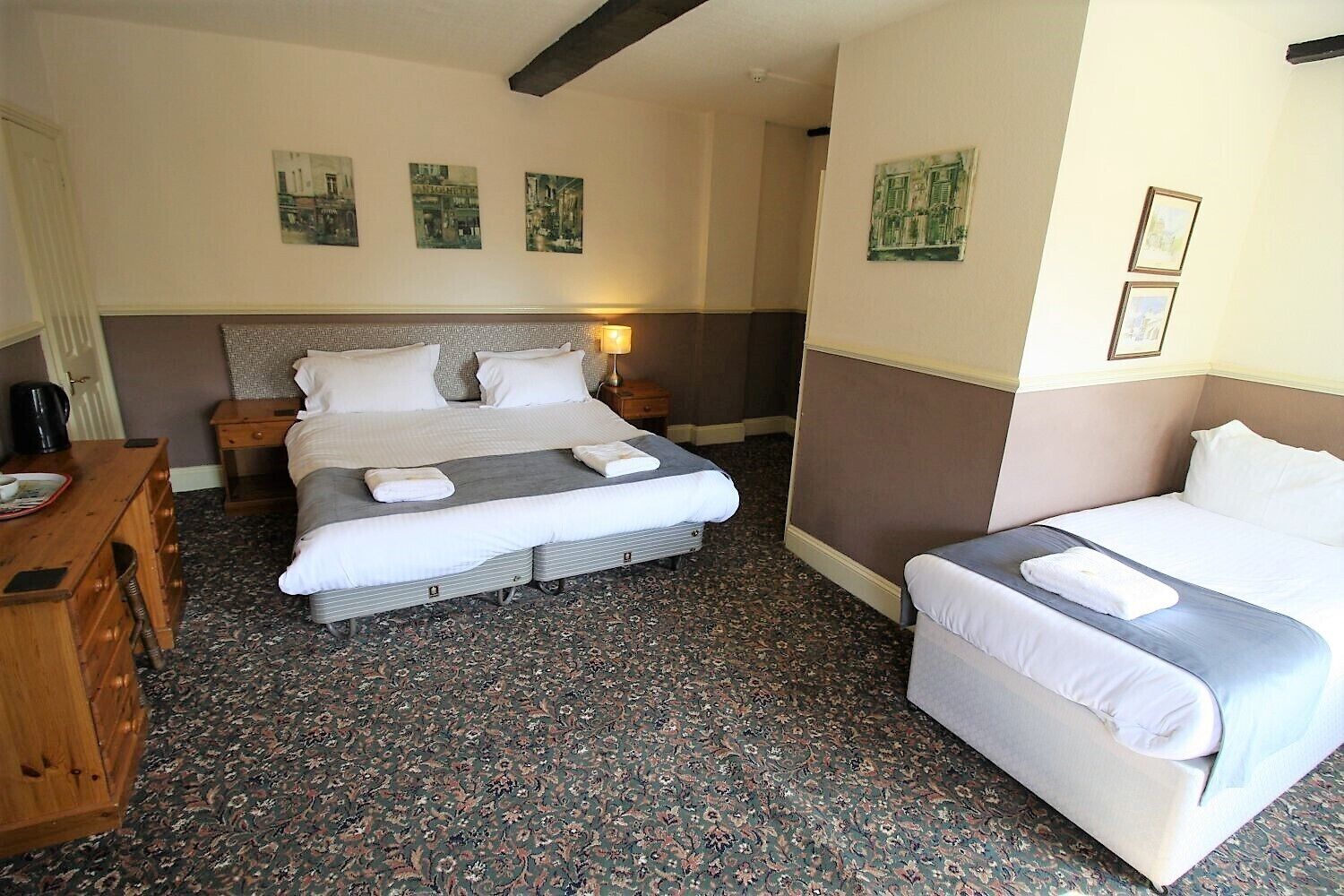 Una habitación de hotel con una cama grande, una cama más pequeña, un aparador de madera y una mesita de noche.