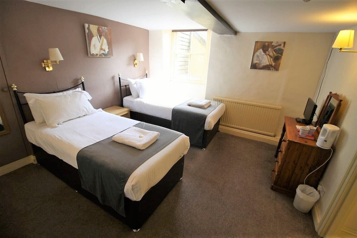 A hotel room with two beds, a desk, a chair, and a radiator.