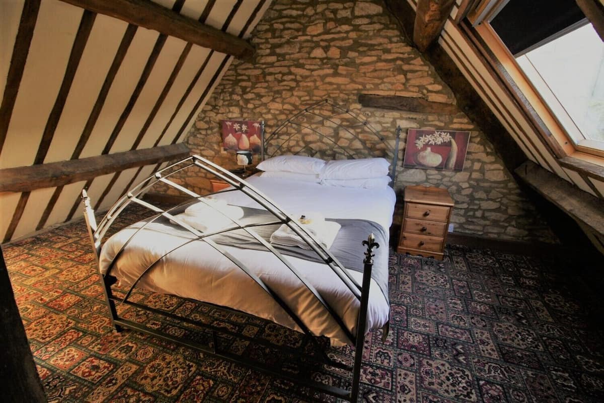 A bedroom with a metal bed frame, a stone wall, a wooden nightstand, and a patterned carpet.