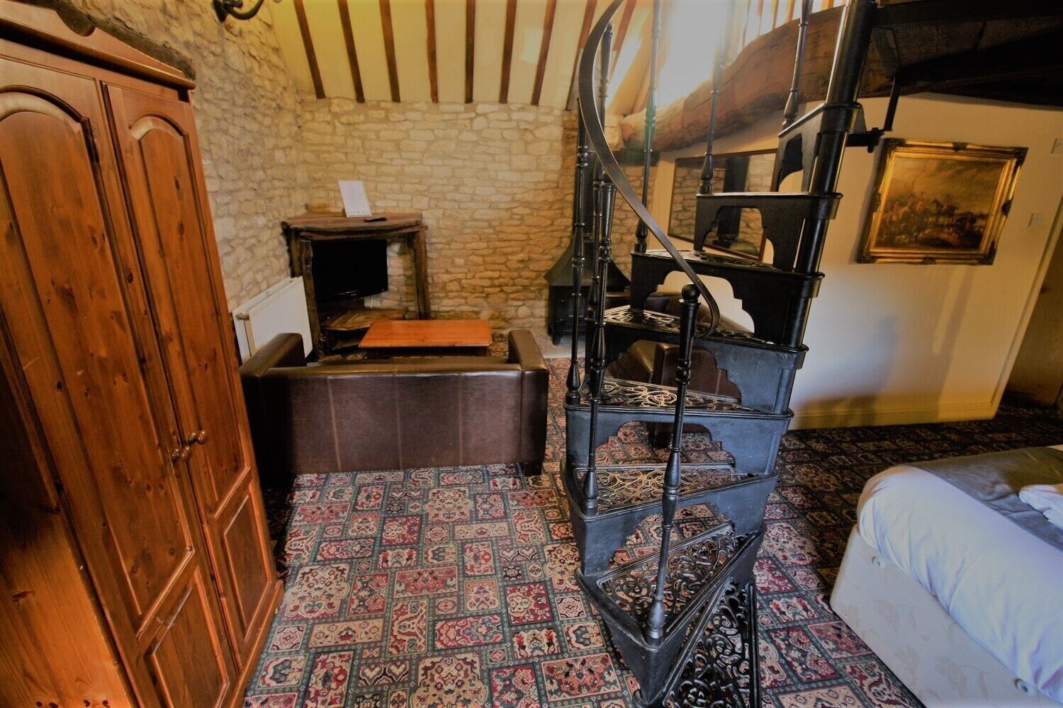 A room with a spiral staircase, a wooden cabinet, a small table with a book, and a patterned carpet.