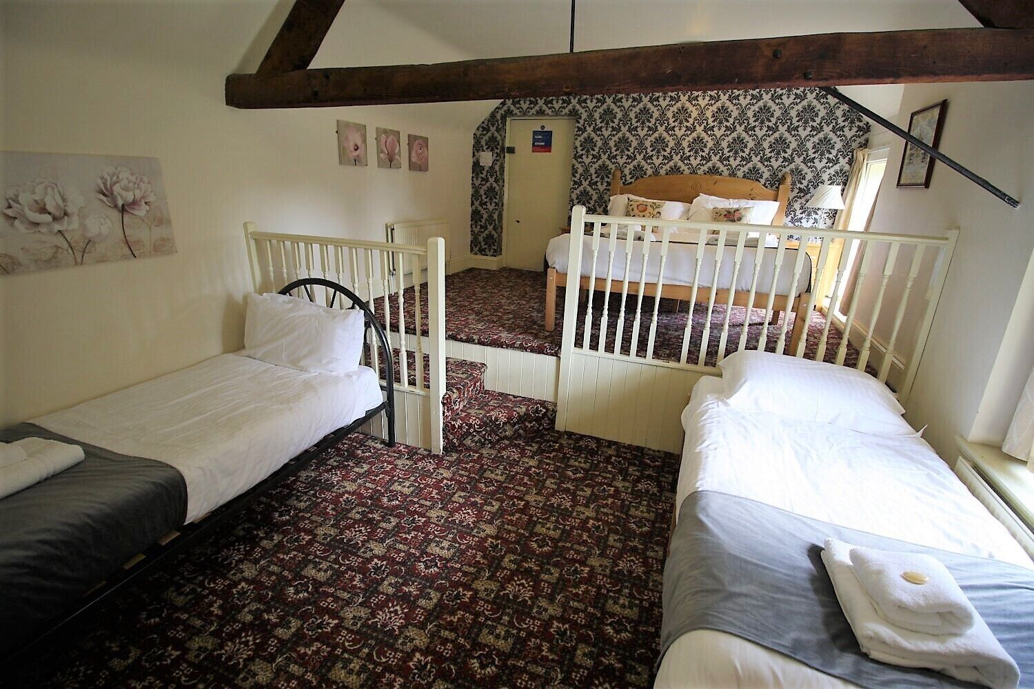 A room with two single beds, a wooden ceiling, floral wallpaper, and a patterned carpet.