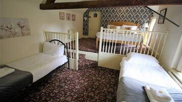 A room with two single beds, a wooden ceiling, floral wallpaper, and a patterned carpet.