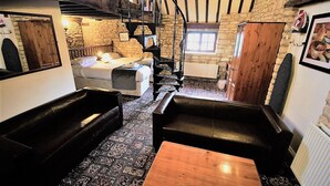 A cozy room with a bed, two leather sofas, a wooden coffee table, and a stone wall. - The Kings Arms Chipping Norton (Chipping Norton)