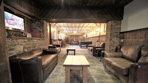 A cozy, rustic lounge area with leather sofas, a wooden coffee table, and a television screen displaying an advertisement. - The Kings Arms Chipping Norton (Chipping Norton)