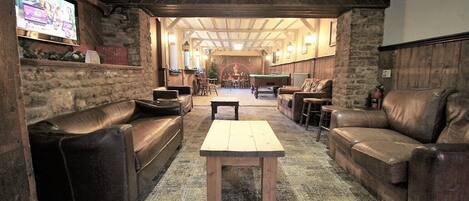 A cozy, rustic lounge area with leather sofas, a wooden coffee table, and a television screen displaying an advertisement.