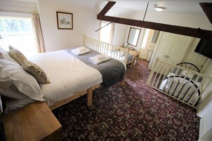 A bedroom with a bed, a wooden nightstand, a small table, a crib, and a patterned carpet.