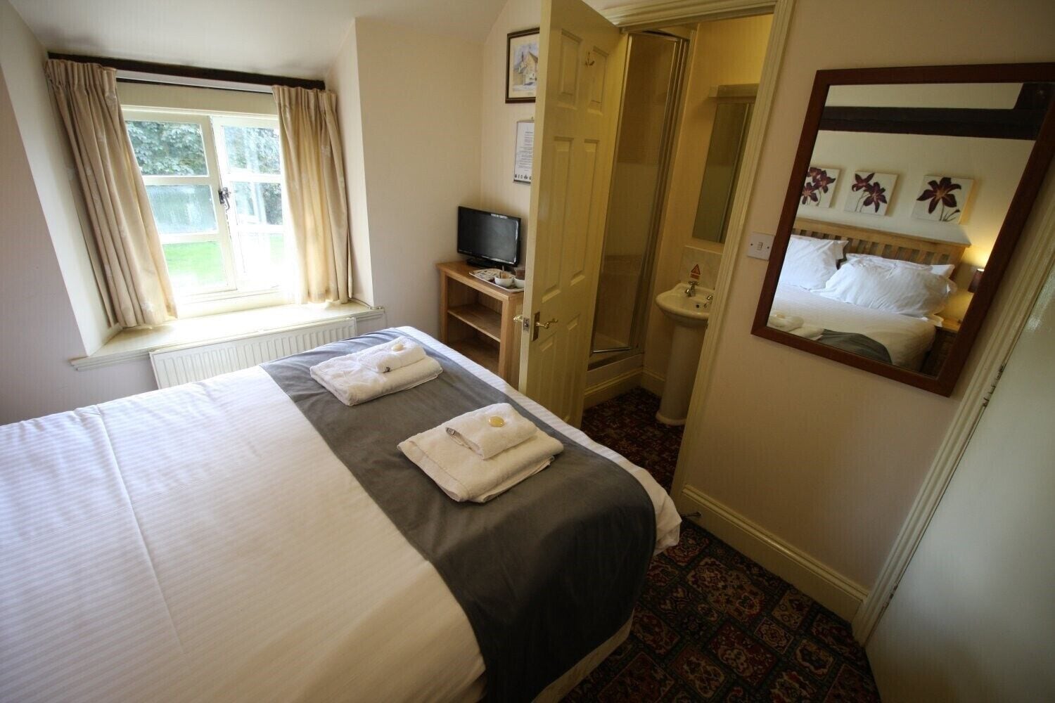 A hotel room with a large bed, a television, a bathroom with a sink, and a mirror.