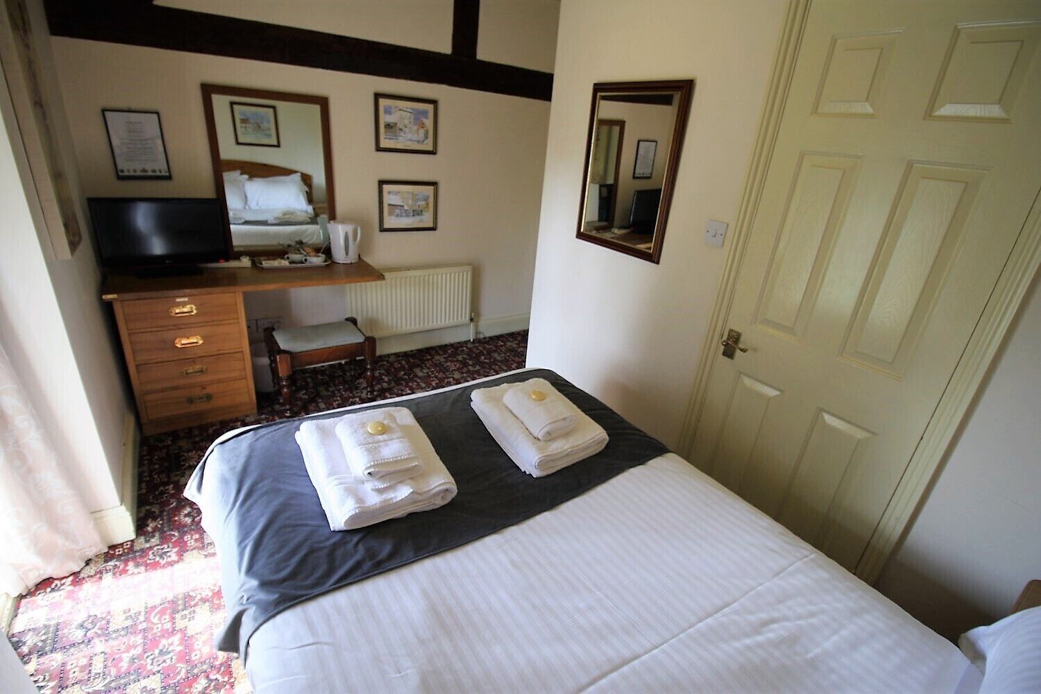 A hotel room with a bed, a desk with a chair, a television, and a door.