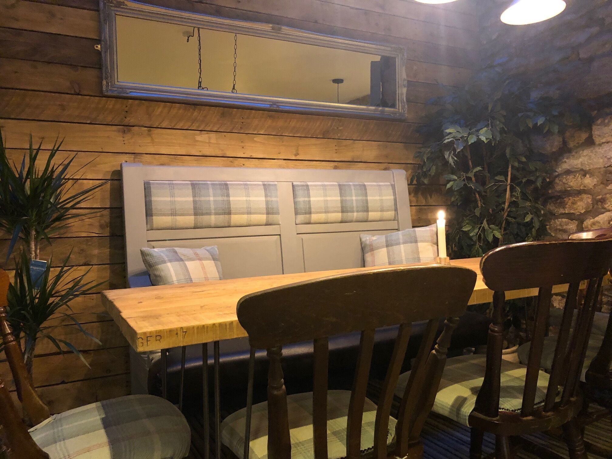 Un interior de madera con una mesa y sillas, un banco con cojines de cuadros y un espejo colgado.