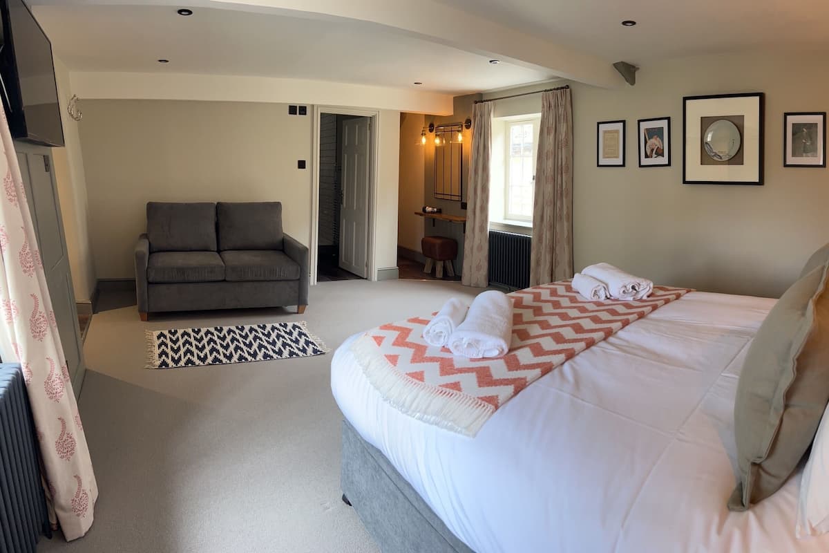 A hotel room with a large bed, a grey sofa, a small table, and a mirror.