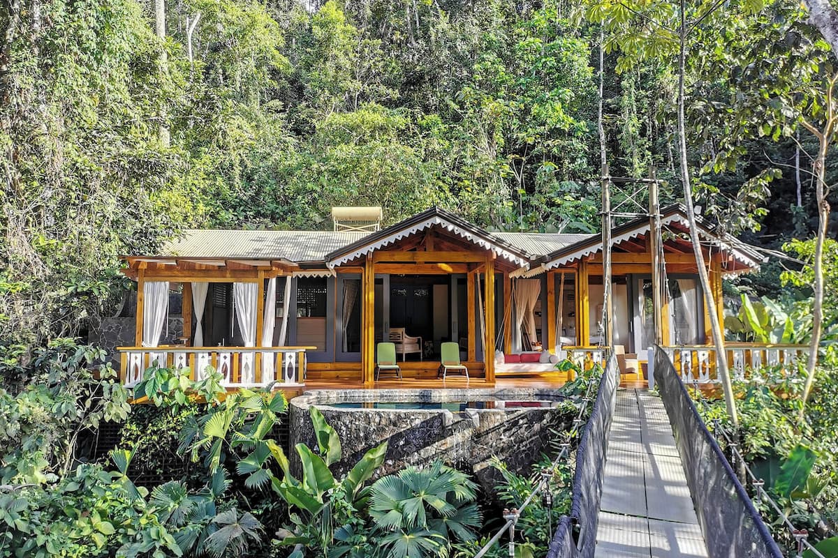 A wooden cabin with a porch and a small pool, surrounded by lush greenery.
