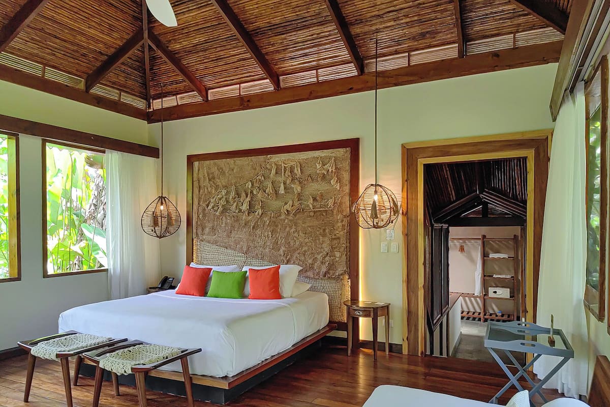 A spacious bedroom with a large bed, wooden flooring, and a ceiling with exposed beams.