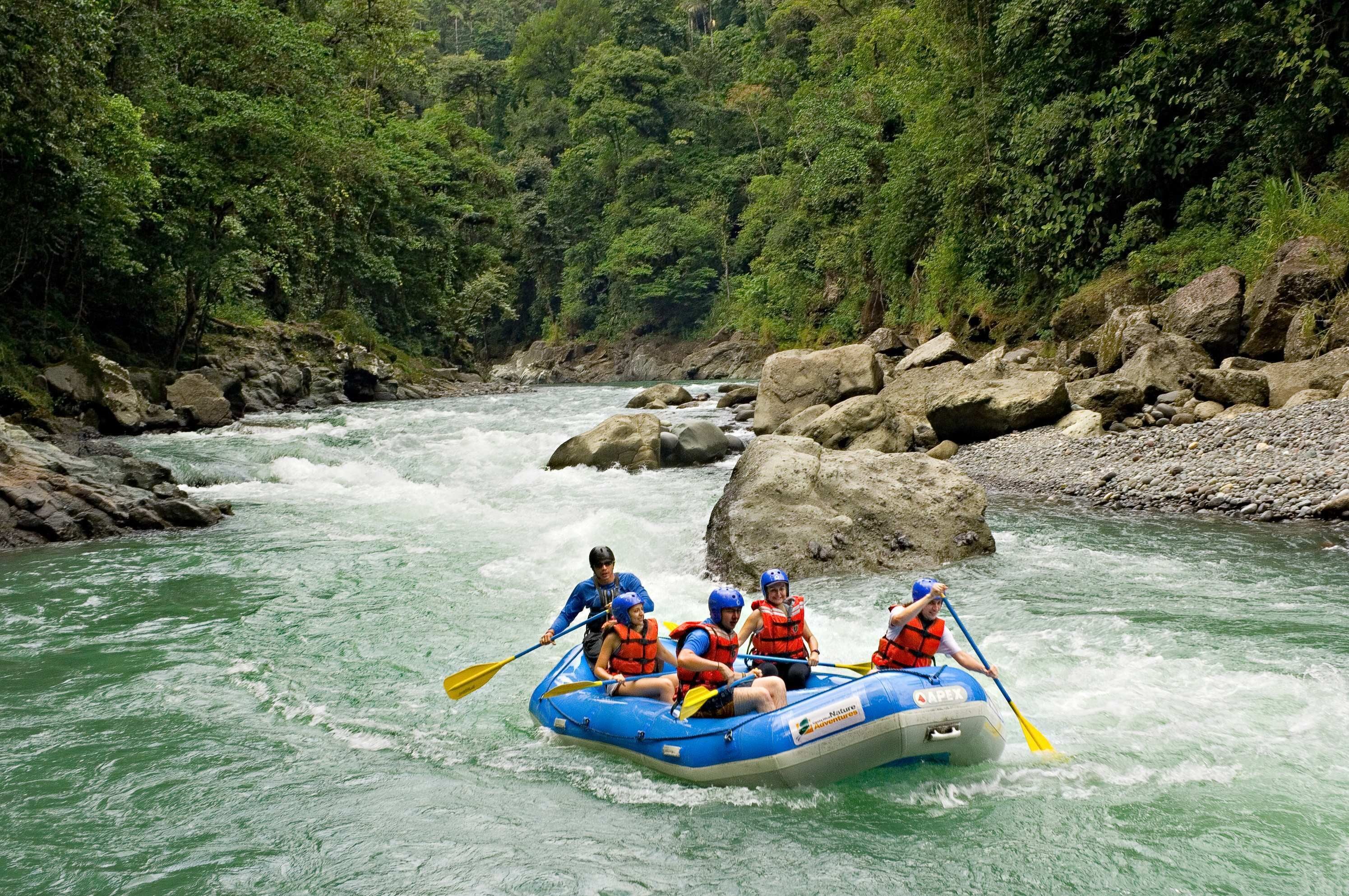 Un grupo de personas en una balsa inflable azul navega por un río rodeado de terreno rocoso y vegetación densa.