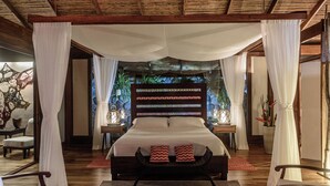 A bedroom with a canopy bed, a stone wall backdrop, and a view of greenery. - Pacuare Lodge by Böëna (Siquirres)