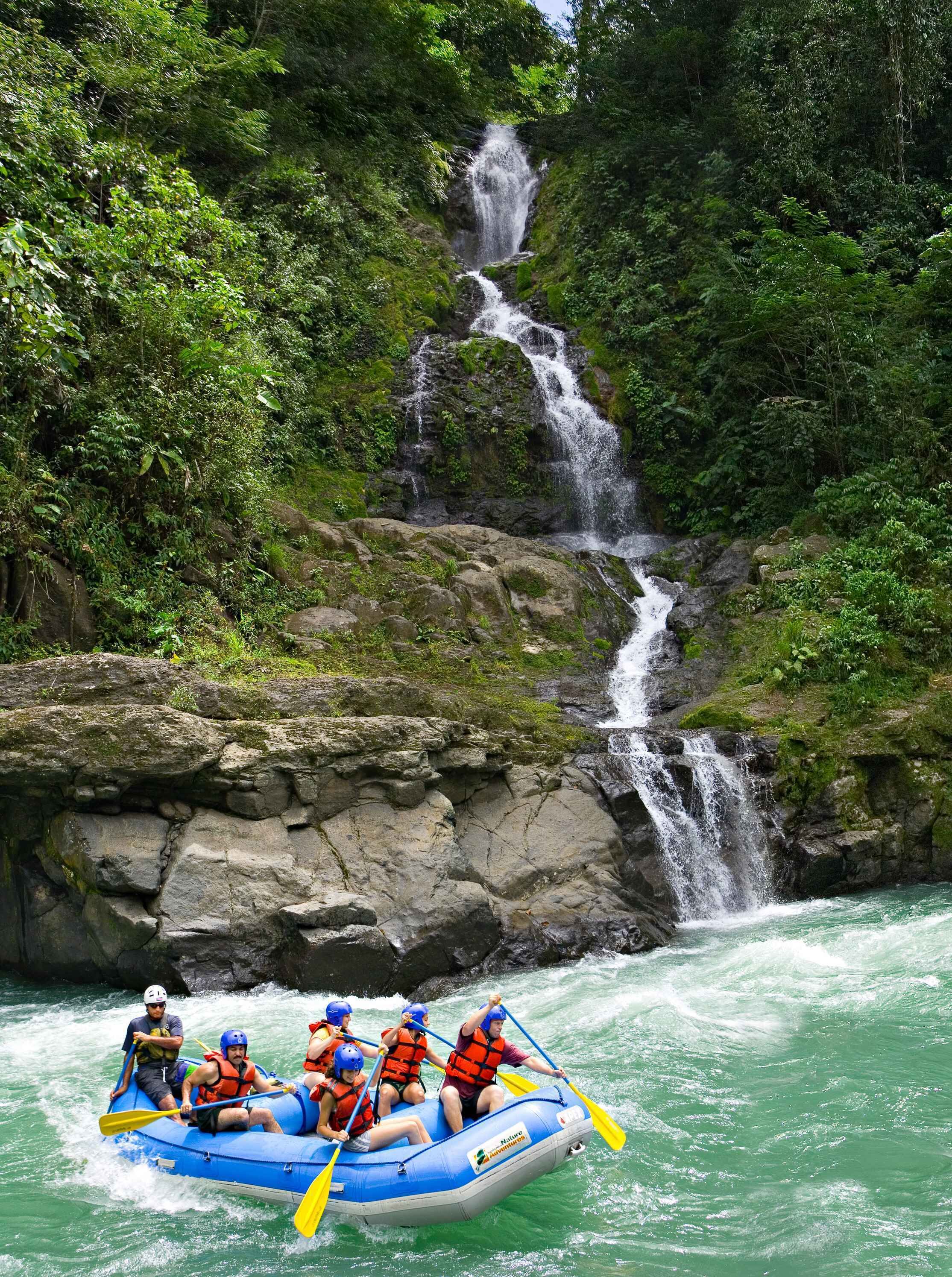 Un gruppo di persone fa rafting su un fiume con una cascata sullo sfondo.