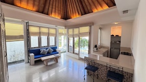 A spacious room with a blue sofa, a dining table, and a kitchen area. - Artemis Villa and Hotel (Seminyak)