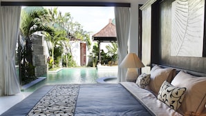 A bedroom with a large bed, a view of a swimming pool, and a tropical garden. - Artemis Villa and Hotel (Seminyak)
