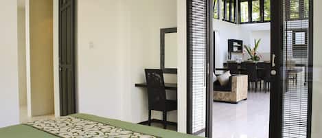 Una habitación de hotel moderna con una cama, un escritorio y un área de comedor visible a través de un vidrio.