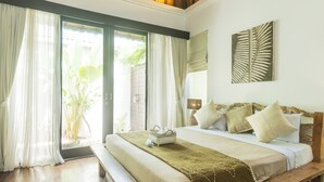 A bedroom with a large bed, a bench, a window with curtains, and a wall-mounted artwork. - Artemis Villa and Hotel (Seminyak)