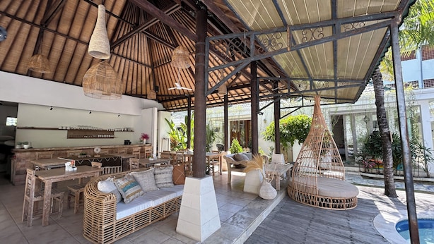 An outdoor covered patio with wooden furniture, a stone bench, and hanging wicker lamps. - Artemis Villa and Hotel (Seminyak)