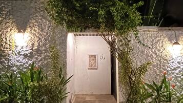 A stone wall entrance with a door labeled "G1", surrounded by potted plants and illuminated by wall-mounted lights.